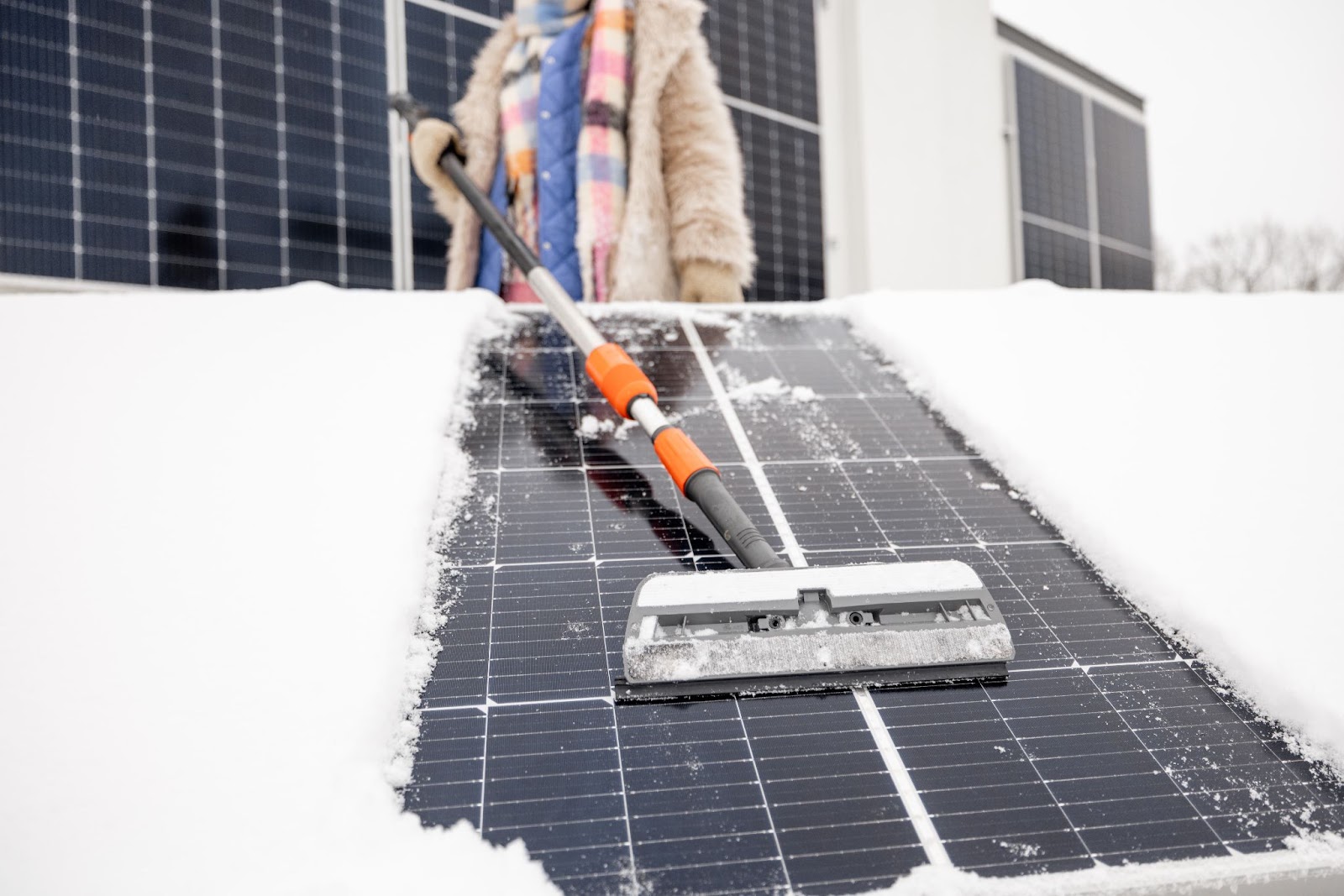 Woman brushing snow off her solar panels off her roof